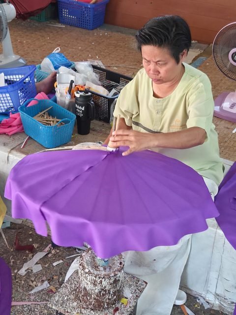 En tenue du centre, une personne met en place une couverture de tissu violet sur une armature, un pinceau à la main