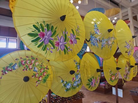 Des ombrelles jaunes ouvertes suspendues dans une salle de vente, peintes d'orchidées, de grues, de fleurs et de papillons