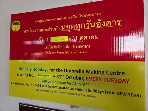 Une affiche rouge et jaune, en thaï et en anglais, qui annonce la fermeture hebdomadaire du mardi de l'Umbrella Making Centre