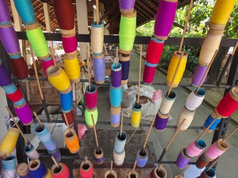 Un râtelier de bobines de bambou garnies de fil aux couleurs vives, dans un atelier ouvert