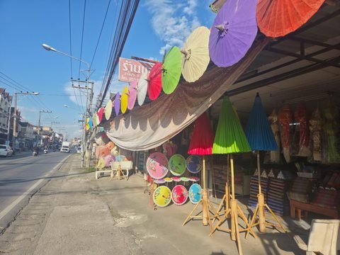 Des ombrelles de couleur suspendues le long de l'auvent d'une boutique et des ombrelles peintes sur des supports, au bord d'une route, sous un ciel bleu