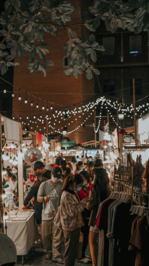 Shoppers browsing between illuminated stalls and clothing rails at a night market