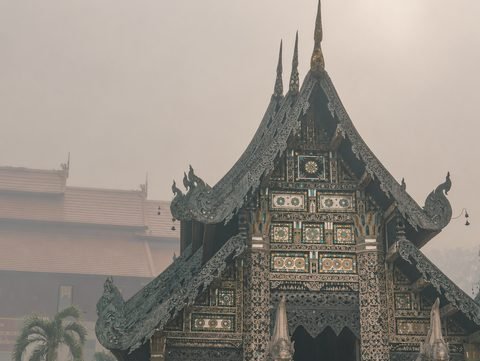 The carved, ornate gable of a Lanna temple hall against a smoke-filled sky