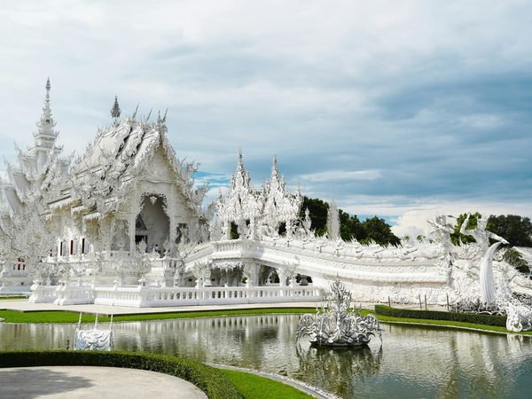 The white plaster and mirrored glass of Wat Rong Khun, the White Temple, above its pond