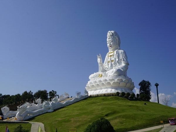 The white Guan Yin statue of Wat Huay Pla Kang seated above a green hillside