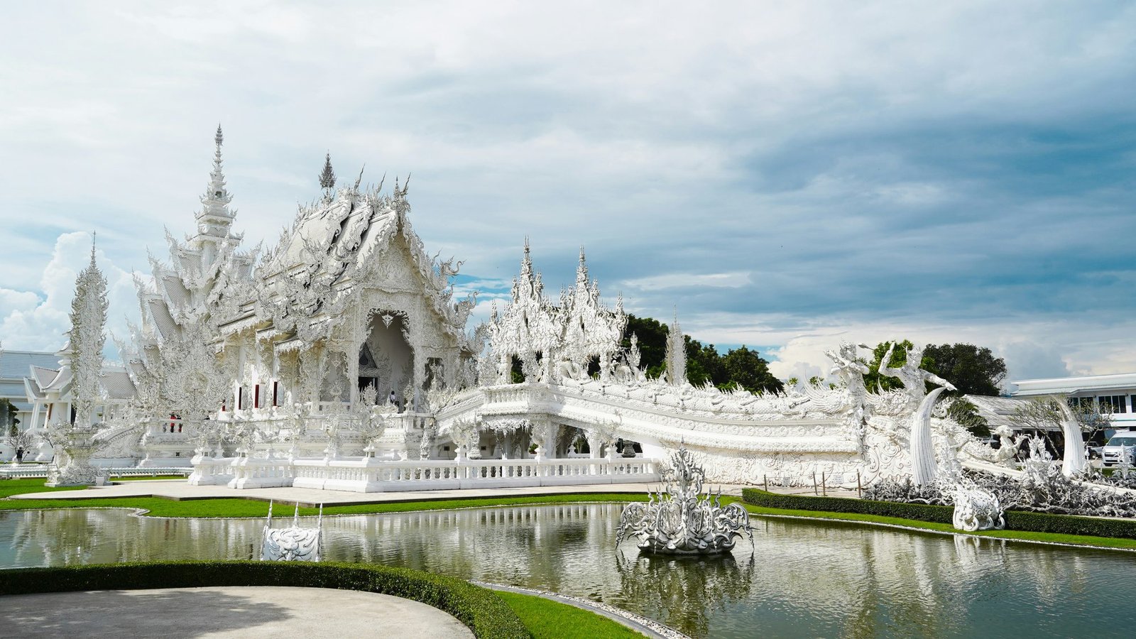 The white plaster and mirrored glass of Wat Rong Khun reflected in the pond in front of it