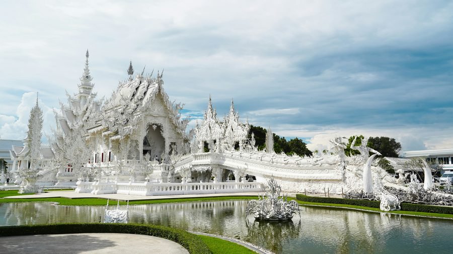 The white plaster and mirrored glass of Wat Rong Khun reflected in the pond in front of it