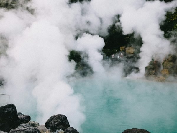 Steam rising off a turquoise hot spring pool ringed with dark rock