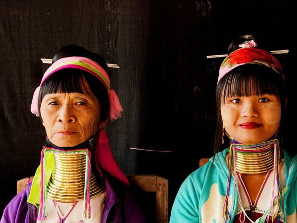 Two Kayan women in traditional dress, wearing the brass neck coils, seated in a village near Chiang Rai