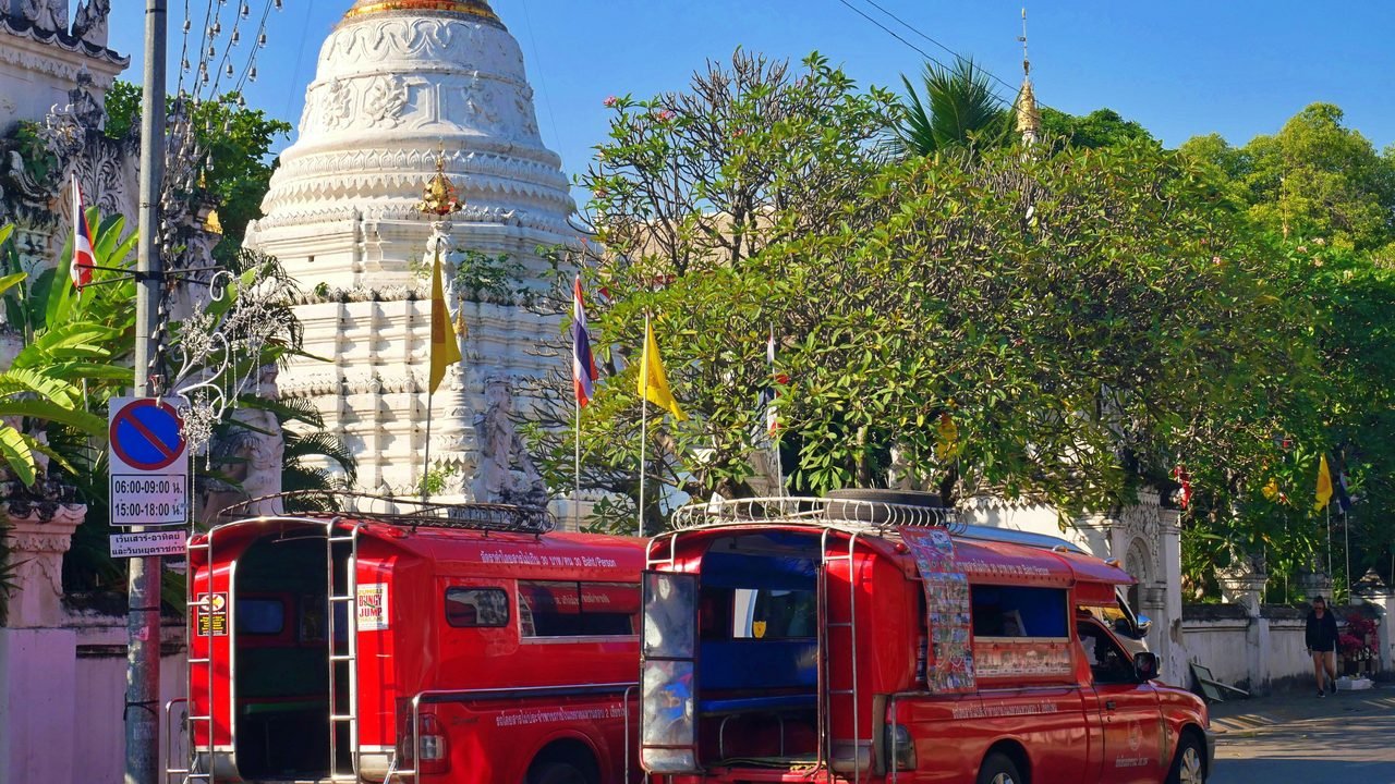 Two red songthaew shared taxis parked outside a white Lanna chedi in Chiang Mai