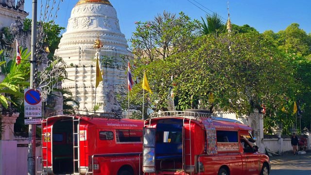Two red songthaew shared taxis parked outside a white Lanna chedi in Chiang Mai