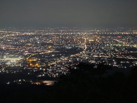 Les lumières de Chiang Mai étalées sur la plaine, la nuit, vues depuis la forêt sombre de la montagne