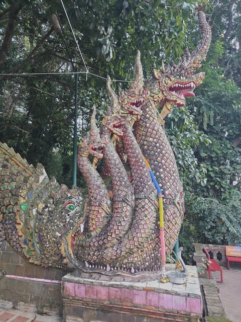 Les têtes du naga au pied de l'escalier, couvertes de miroirs et d'une mosaïque rouge, or et verte, au-dessus de la gueule d'une créature plus grande au museau recourbé, d'où sort le corps du serpent