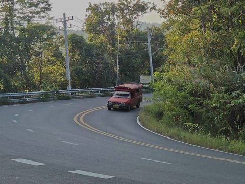 Un songthaew rouge dans un virage serré de la route de montagne, entre une glissière de sécurité et la forêt