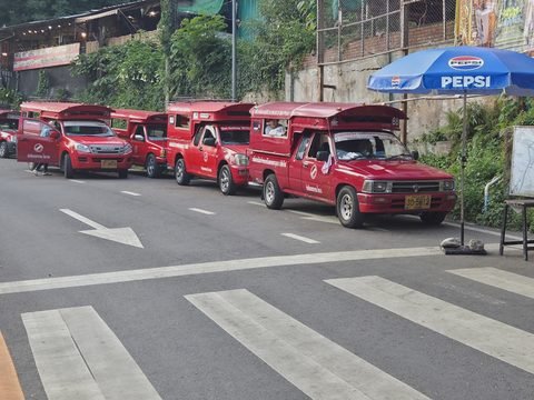 Une file de songthaews rouges garés le long de la route au pied de l'escalier du temple, près d'un parasol bleu aux couleurs de Pepsi, un passage piéton au premier plan
