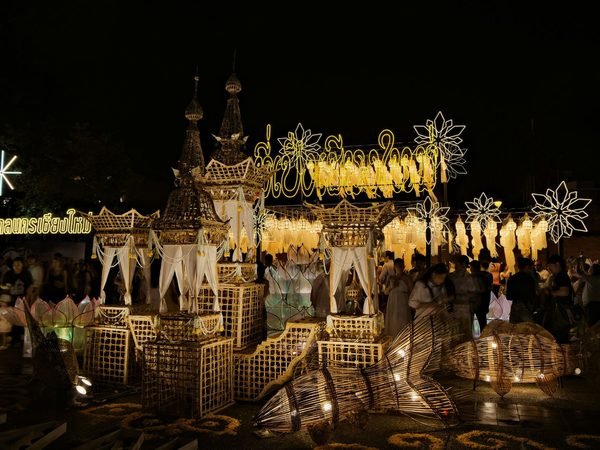 A lantern and bamboo installation lit up at night, with people walking around it and an illuminated Chiang Mai Municipality sign in Thai on the left