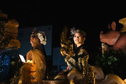 Two performers in gold costumes and ornate headdresses on an illuminated float at night