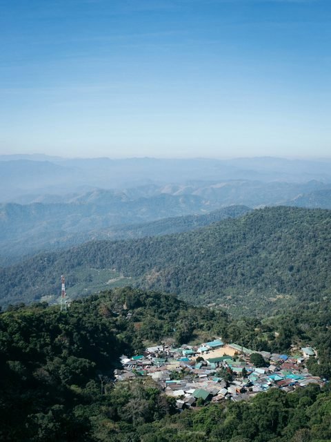 A hill village on a forested ridge, with mountain ranges receding into the haze