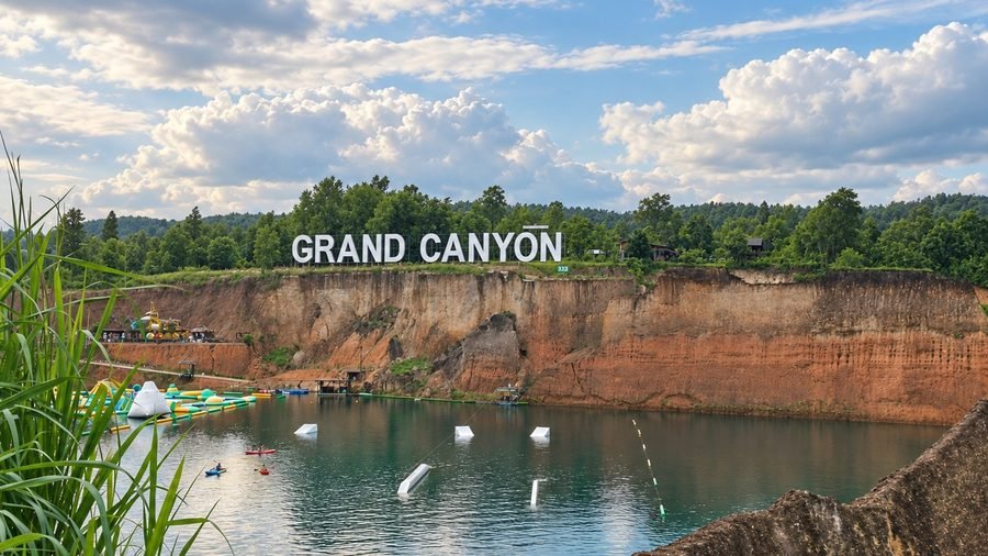 The white GRAND CANYON sign on the clifftop above the flooded quarry at Hang Dong, kayaks and an inflatable course on the green water below