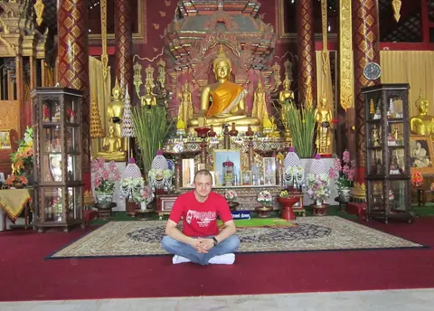 Gregory sitting cross-legged on a red carpet in front of a temple altar with golden Buddha statues