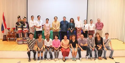 Group photo of about twenty people in a hall, some seated in the front row and others standing behind, with a Thai flag on the left