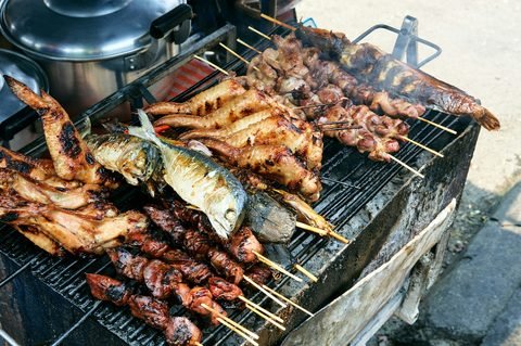 Skewers of meat and whole fish grilling over charcoal at a street stall