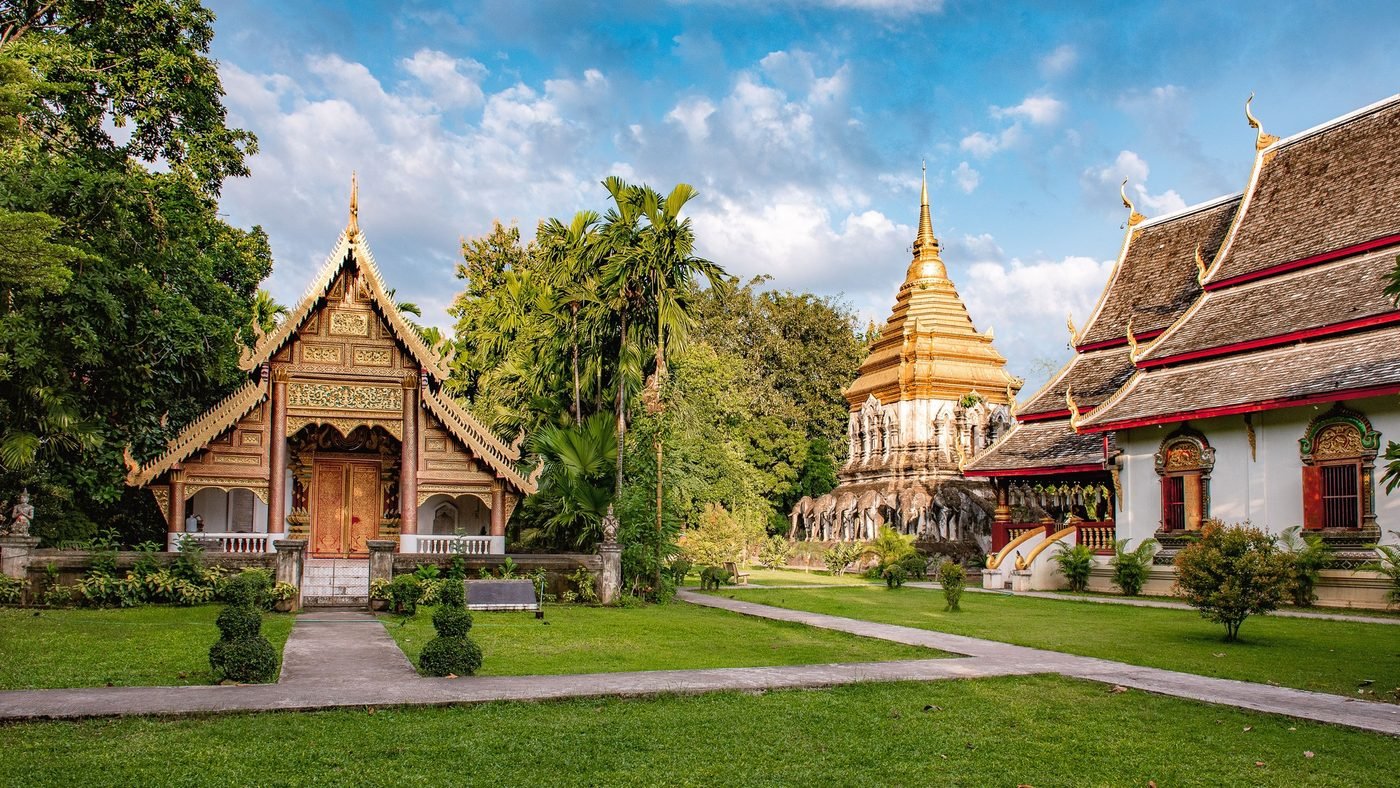 Wat Chiang Man in Chiang Mai's old city: a gilded chedi on a base of sculpted elephants, between two temple halls and a lawn