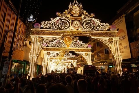 A dense crowd filling a street at night beneath a succession of brightly lit decorative arches