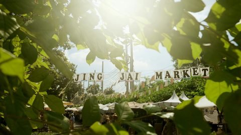 The Jing Jai Market sign seen through leaves above the market stalls