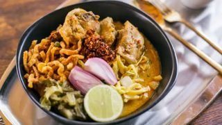 A bowl of chicken khao soi with crisp noodles, pickled mustard greens, shallot and lime