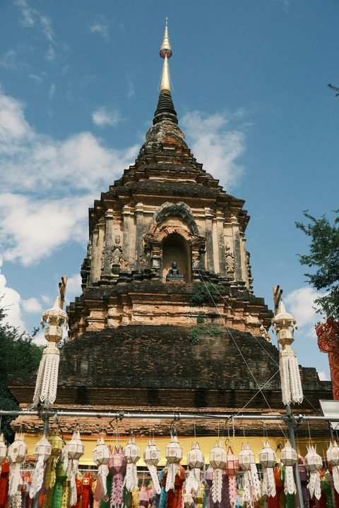 A brick chedi with a gilded spire, above a long line of white hanging lanterns with paper tails
