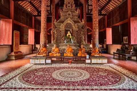Monks seated before the principal Buddha image inside a teak wihan