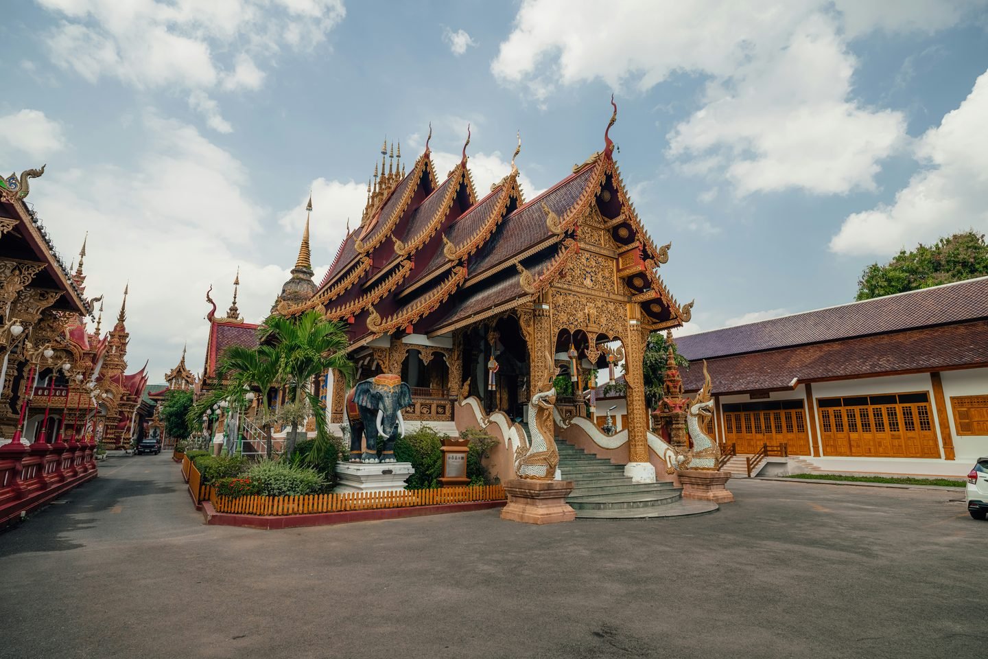 A Lanna assembly hall with tiered roof and deep eaves, cars parked in the temple courtyard