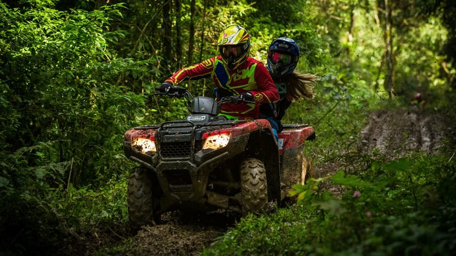 Two riders in helmets on a red quad bike on a muddy forest track