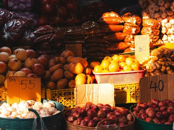 A market stall stacked with fruit and vegetables in baskets and crates, handwritten prices in front