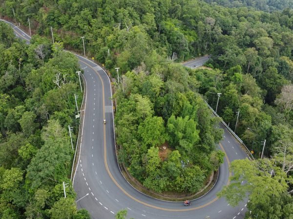 Aerial view of a road looping through a tight hairpin bend in dense forest, with two motorbikes on it