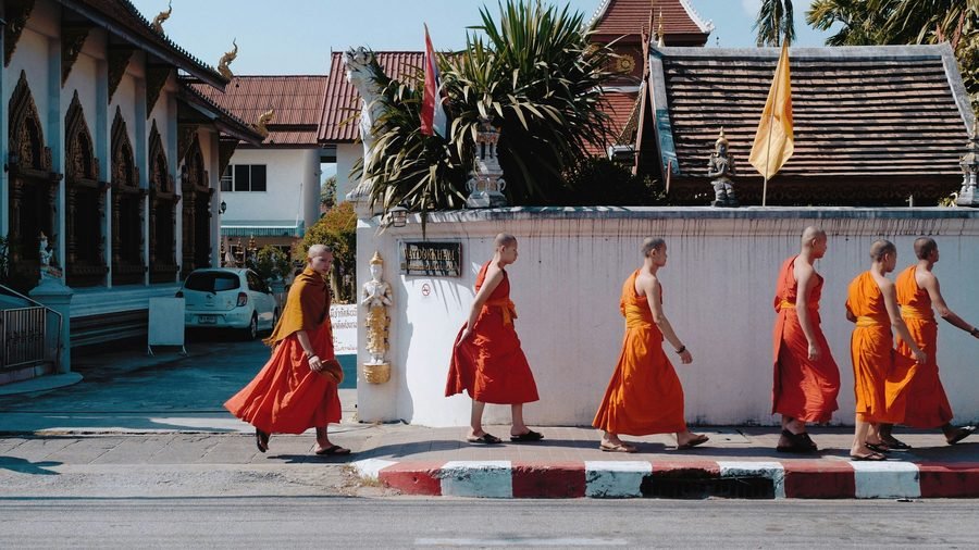 A file of monks in orange robes walking along a temple wall in the old city of Chiang Mai