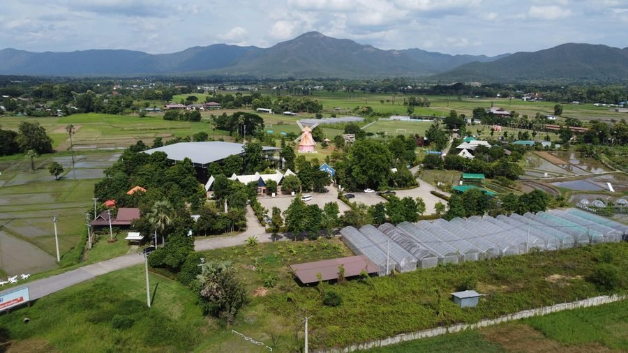 An organic farm seen from the air: greenhouses, planted beds and rice paddies, with mountains behind