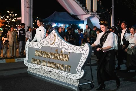 A night procession on a city street, led by an ornate white sign reading Chiang Mai Municipality, with people in formal dress walking behind