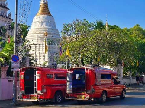 Two red songthaews, shared pick-up taxis, parked on a Chiang Mai street beside a white temple chedi