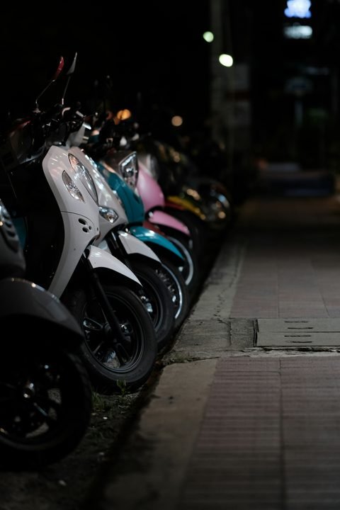 A row of scooters parked along a pavement at night