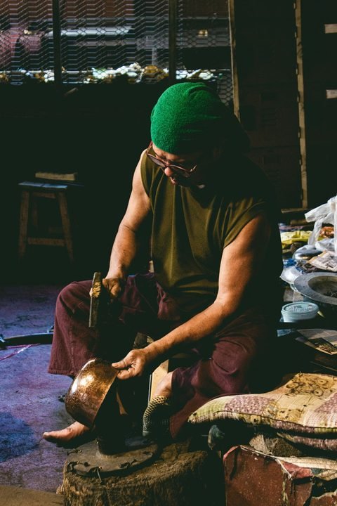 A craftsman hand-beating a metal bowl in a workshop