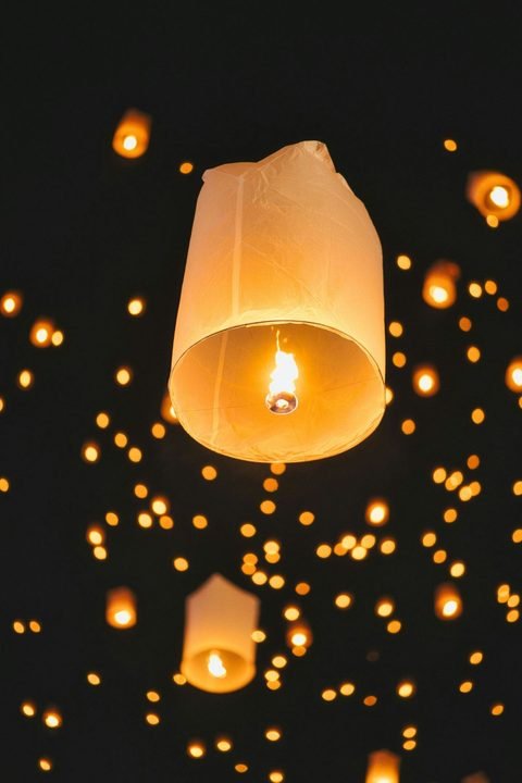 A single paper sky lantern in the foreground, with many more lit lanterns rising in the dark sky