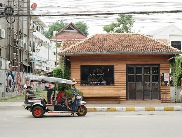 A wooden coffee shop on a Chiang Mai street corner, a tuk-tuk waiting at the kerb in front of it