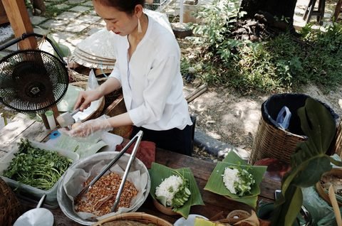 A cook assembling dishes on banana leaves at an outdoor prep table