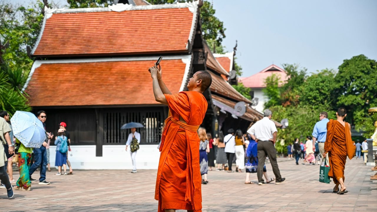 A monk in orange robes photographing the teak roof of a Lanna temple in the old city of Chiang Mai