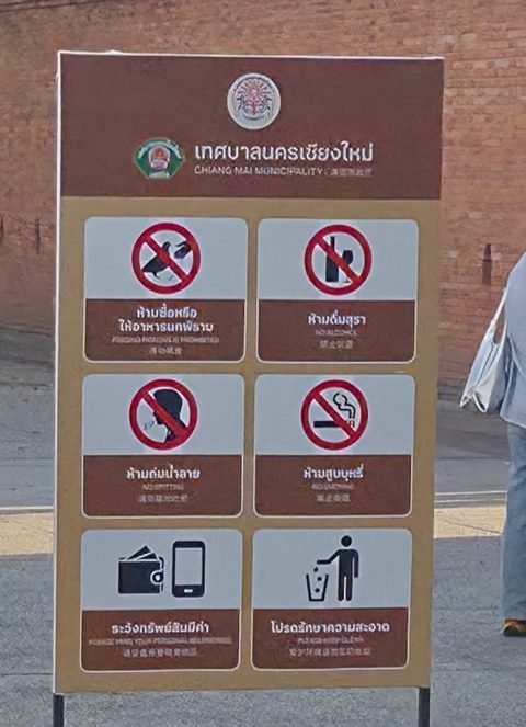 Chiang Mai Municipality sign on Tha Phae Gate square with six pictograms: no buying pigeon food or feeding the pigeons, no alcohol, no spitting, no smoking, mind your valuables, keep the area clean
