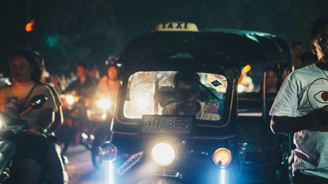 A tuk-tuk in Chiang Mai traffic at night, headlights on, scooters on either side