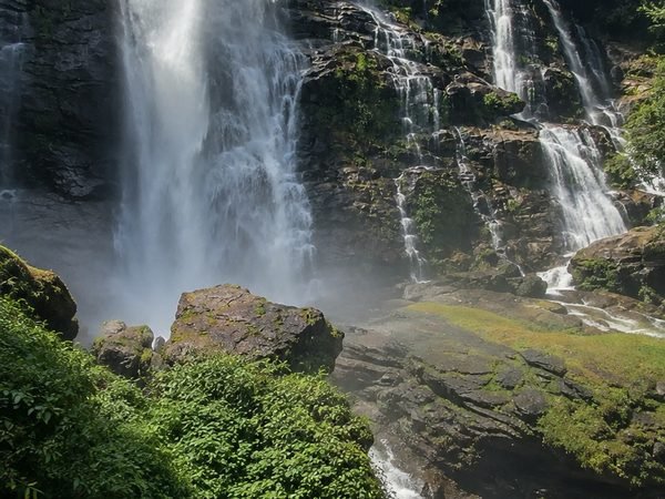 The Wachirathan waterfall dropping in a wide curtain onto black rock, spray hanging over the basin