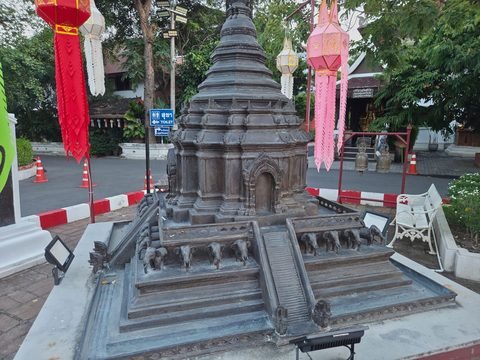 A dark bronze model of the chedi on a low plinth in the compound: elephants along the terrace, a stairway with nagas at its foot, and the upper tiers rising out of the frame
